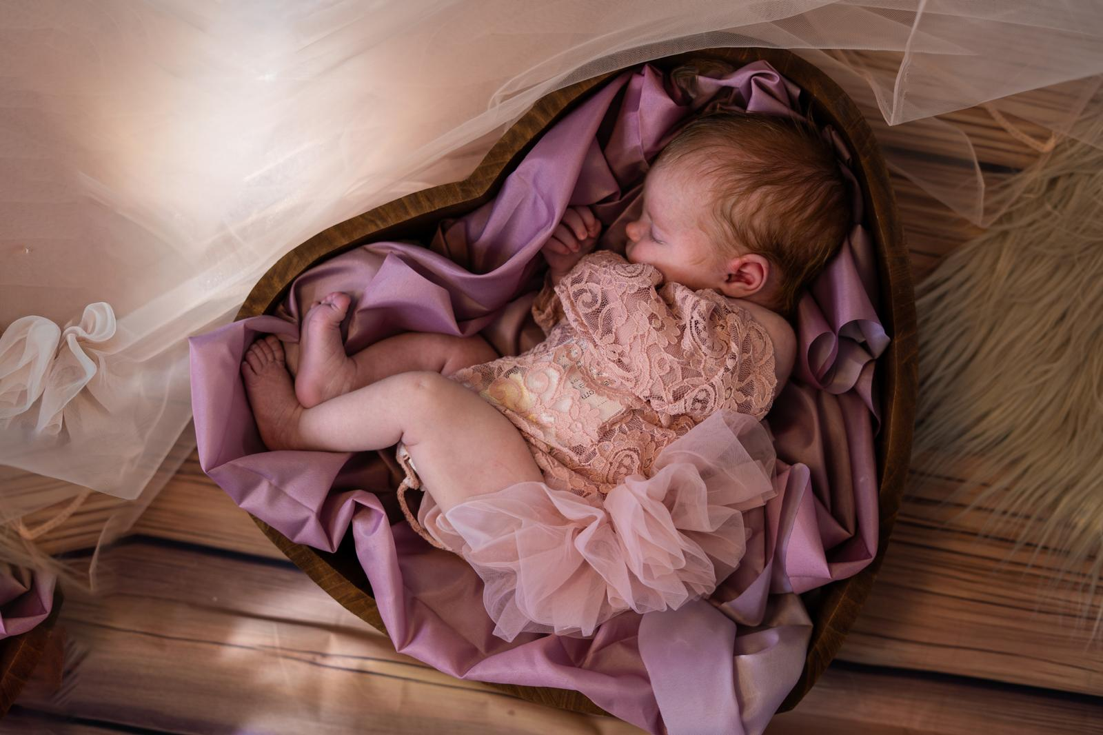 Newborn in heart-shaped bowl with blush silks