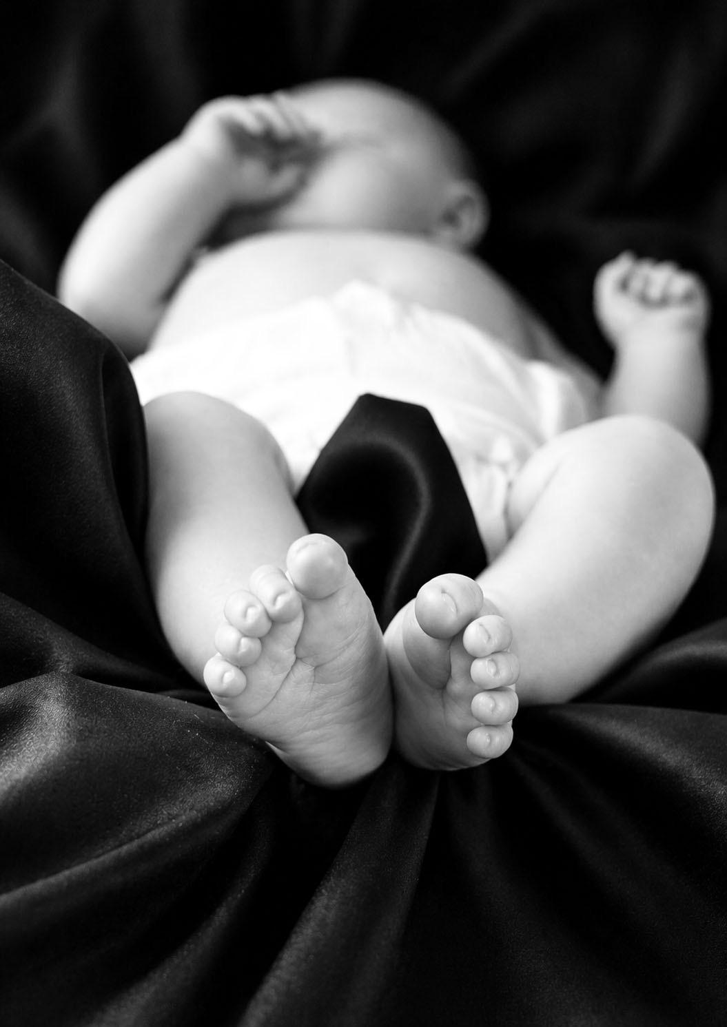 Newborn feet on dark satin, black and white