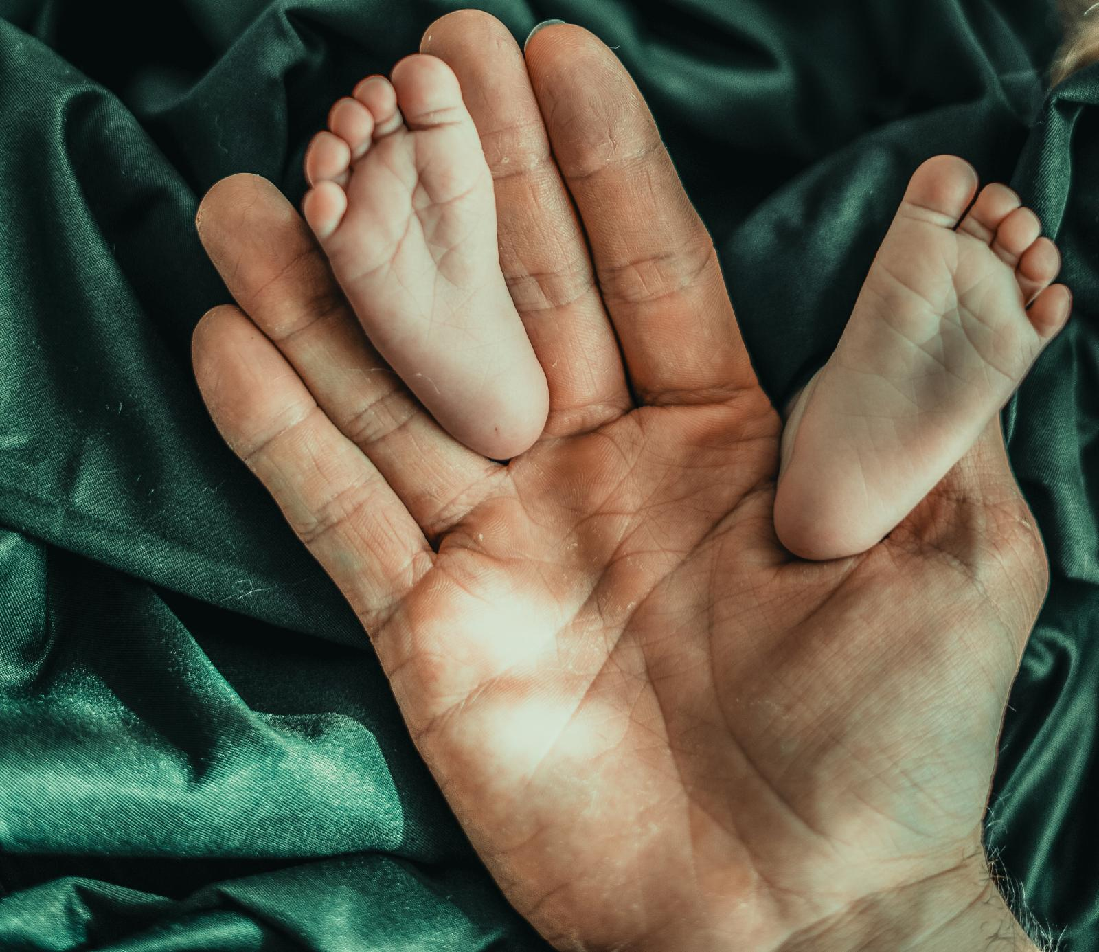 Baby feet on father's palm against green satin